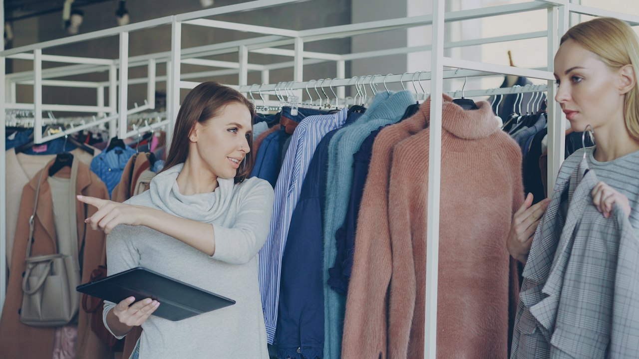 Portage salarial consultant retail : deux femmes avec une tablette devant un portant de vêtements en boutique